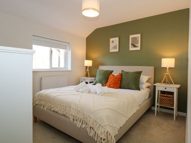 A bedroom with a bed with pillows and rolled towels beside two bedside tables with lamps at Craig y Llan in Beddgelert