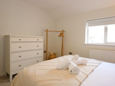 A bedroom with a bed and rolled towels a white chest of drawers and a wooden clothes rack at Craig y Llan in Beddgelert
