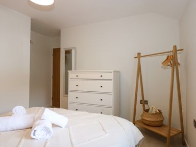 A bedroom with a white chest of drawers a wooden clothes rack with hangers and a basket and a bed with rolled white towels at Craig y Llan in Beddgelert