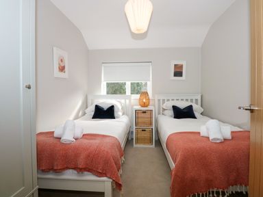 A bedroom with two single beds side by side with orange blankets and rolled white towels on top at Craig y Llan in Beddgelert