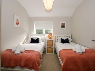 A bedroom with two single beds with orange blankets a lamp and two framed pictures at Craig y Llan in Beddgelert
