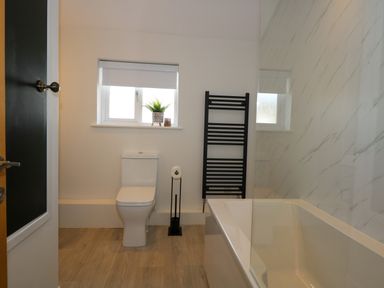 A bathroom with a white toilet a black towel rack a bathtub and a small window with a plant and a candle on the sill at Craig y Llan in Beddgelert