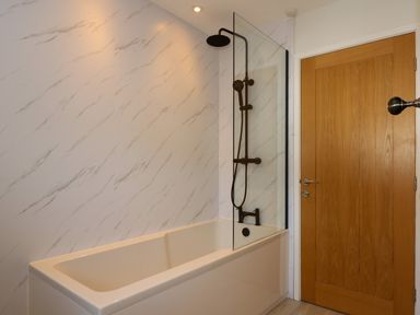A bathroom with a bathtub and a black shower fixture next to a wooden door at Craig y Llan in Beddgelert