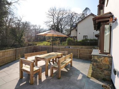 An outdoor patio area with wooden benches and a table with an umbrella surrounded by a wooden fence at Craig y Llan in Beddgelert