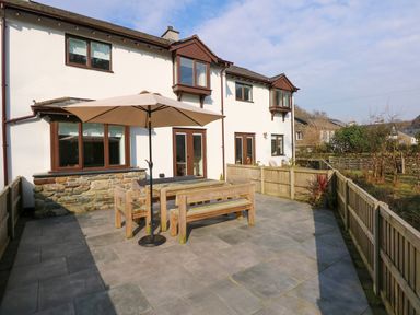 A patio with wooden outdoor furniture and an umbrella outside a white house with brown windows at Craig y Llan in Beddgelert