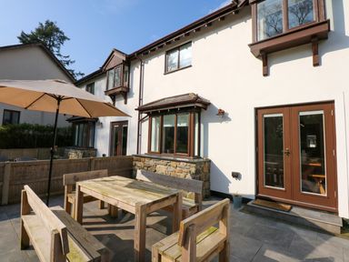 An outdoor patio with wooden benches and table under a large umbrella outside a white house with brown window frames and doors at Craig y Llan in Beddgelert