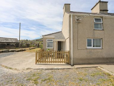 The exterior of a house with a small fenced patio area and surrounding gravel and grass at Cwm Ceiliog Annex in Llanaelhaearn near Trefor
