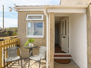 A small outdoor seating area with two chairs and a table next to an open door at Cwm Ceiliog Annex in Llanaelhaearn near Trefor