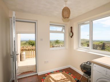A utility room with a round rug a charcoal grill a washing machine and windows overlooking a rural landscape at Cwm Ceiliog Annex Llanaelhaearn near Trefor