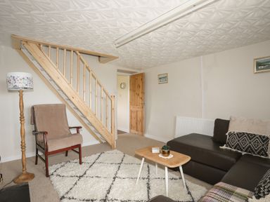 A living room with a wooden staircase a floor lamp an armchair a coffee table and a sofa at Cwm Ceiliog Annex Llanaelhaearn near Trefor