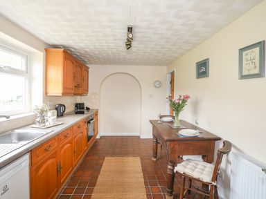 A kitchen with wooden cabinets a dining table with flowers and two place settings at Cwm Ceiliog Annex in Llanaelhaearn near Trefor