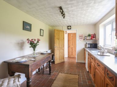 A kitchen with wooden cabinets a wooden table with flowers set for dining and tiled floor at Cwm Ceiliog Annex in Llanaelhaearn near Trefor