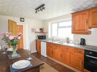 A kitchen with wooden cabinets a dining table set with plates glasses and flowers and kitchen appliances at Cwm Ceiliog Annex Llanaelhaearn near Trefor