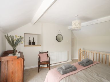 A bedroom with a bed with folded towels a wooden dresser with flowers a chair with a cushion a round mirror and a wooden railing at Cwm Ceiliog Annex in Llanaelhaearn near Trefor