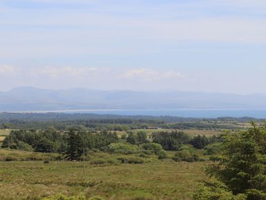 A rural landscape with fields and trees and a body of water with mountains in the background at Cwm Ceiliog Annex in Llanaelhaearn near Trefor