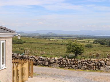 A rural landscape with a stone wall fence and a wooden gate next to a building at Cwm Ceiliog Annex Llanaelhaearn near Trefor