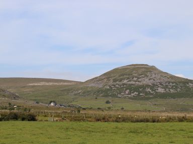 A grassy field with a stone wall and a fenced area near a hill at Cwm Ceiliog Annex in Llanaelhaearn near Trefor