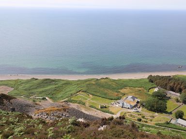 A coastal view with a beach green hills and buildings at Cwm Ceiliog Annex Llanaelhaearn near Trefor