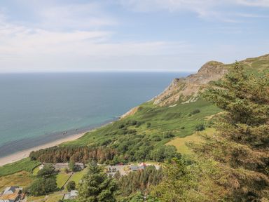 A coastal landscape with a beach, green hills, trees, buildings, and a parking area at Cwm Ceiliog Annex in Llanaelhaearn near Trefor