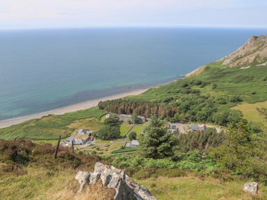 A coastal landscape with a beach, grassy hills, and buildings near the shore at Cwm Ceiliog Annex in Llanaelhaearn near Trefor