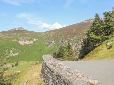 A winding mountain road with a stone wall and green hills with trees at Cwm Ceiliog Annex in Llanaelhaearn near Trefor