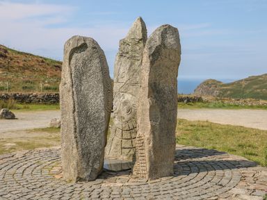 Three standing stone slabs with engraved patterns on a circular paved area outdoors on a hillside with distant hills and sky at Cwm Ceiliog Annex in Llanaelhaearn near Trefor