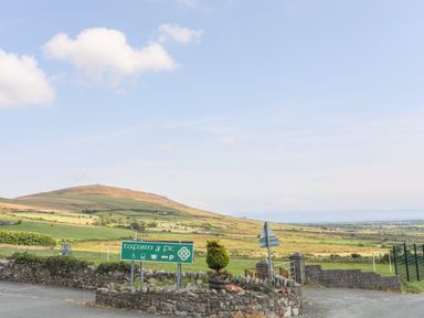 A countryside landscape with a green signpost and stone wall near Cwm Ceiliog Annex in Llanaelhaearn near Trefor