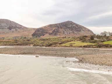 A rocky shoreline with a small wave on water and hills in the background at Cwm Ceiliog Annex in Llanaelhaearn near Trefor