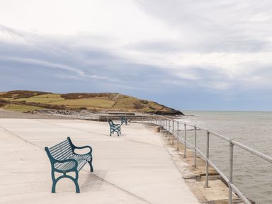 A concrete pier with metal railings and green benches overlooking the sea with grassy hills in the background at Cwm Ceiliog Annex in Llanaelhaearn near Trefor