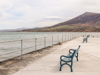 Benches on a concrete pier by the sea with a railing and hills in the background at Cwm Ceiliog Annex in Llanaelhaearn near Trefor