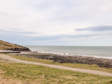 A rocky shore with a grassy path and sea under a cloudy sky at Cwm Ceiliog Annex in Llanaelhaearn near Trefor