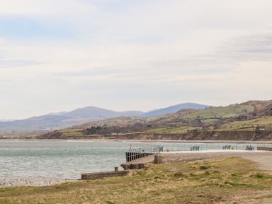 A seafront with benches and railings overlooking a body of water with hills in the background at Cwm Ceiliog Annex in Llanaelhaearn near Trefor