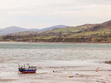 A small boat on a sandy shore with water and hills in the background at Cwm Ceiliog Annex in Llanaelhaearn near Trefor
