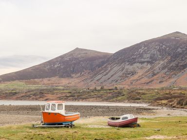 Two small boats on a grassy shore with mountains in the background at Cwm Ceiliog Annex in Llanaelhaearn near Trefor