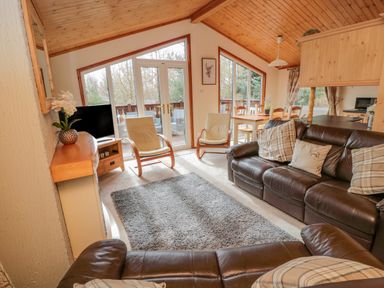 A living room with leather sofas two chairs a dining table and large windows at 4 The Oaks in Swarland