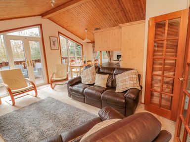 A living room with leather sofas and armchairs next to a dining table and glass doors at 4 The Oaks in Swarland