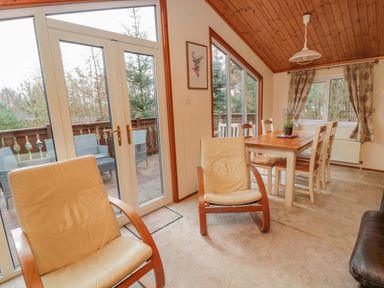 A dining area with a wooden table and chairs and two beige armchairs near glass doors at 4 The Oaks in Swarland