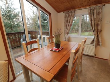 A dining room with a wooden table and six chairs by large windows and glass doors at 4 The Oaks in Swarland