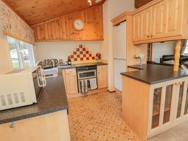 A kitchen with wooden cabinets a refrigerator an oven a microwave and a window at 4 The Oaks in Swarland