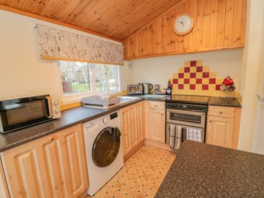 A kitchen with wooden cabinets washing machine microwave and a stove at 4 The Oaks in Swarland