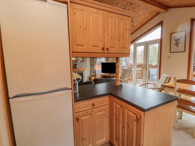 A kitchen area with a refrigerator wooden cabinets black countertop and a view of a living room with a television and chairs at 4 The Oaks in Swarland