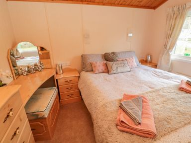 A bedroom with a double bed, bedside tables, a dressing table with a mirror, and folded towels on the bed at 4 The Oaks in Swarland