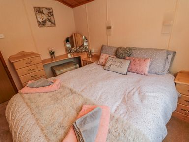 A bedroom with a double bed cushions towels on bed and wooden dressers at 4 The Oaks in Swarland