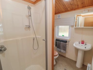 A bathroom with a shower, a toilet, a sink, a window with a blind, and towels hanging on a rail at 4 The Oaks in Swarland