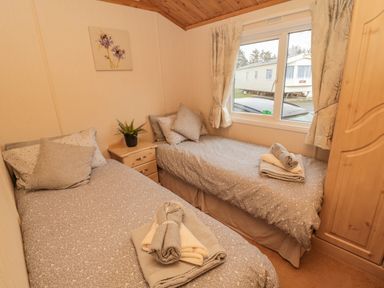 A bedroom with two single beds each with folded towels a nightstand with a plant a window with curtains and a wooden wardrobe at 4 The Oaks in Swarland