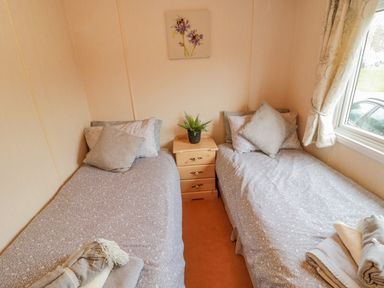 A bedroom with two single beds and a wooden nightstand with a plant between them at 4 The Oaks in Swarland
