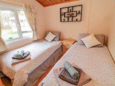 A bedroom with two single beds a wooden nightstand and a window at 4 The Oaks in Swarland