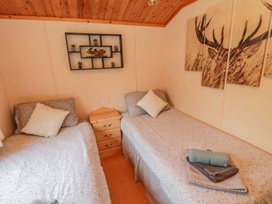 A bedroom with two single beds a wooden nightstand between them and wall art of a deer at 4 The Oaks in Swarland