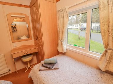 A bedroom with a single bed next to a window a wooden wardrobe and a dressing table with a stool at 4 The Oaks in Swarland