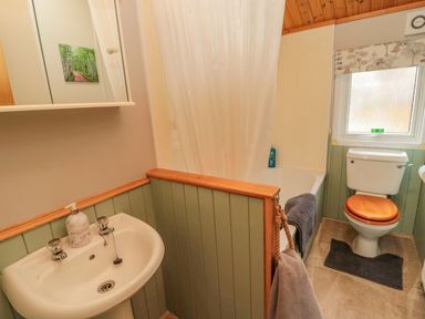 A bathroom with a sink a bathtub with a shower curtain and a toilet with a wooden seat at 4 The Oaks in Swarland